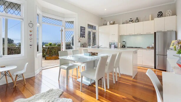 A modern kitchen with white cabinetry, a stainless steel refrigerator, and a dining area with a white table and chairs. - Parnell Home With Stunning Views (Auckland)