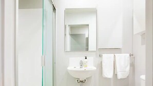 Een badkamer met een douchecabine van glas, een witte wastafel met een spiegel erboven en een toilet met twee witte handdoeken aan een rek.