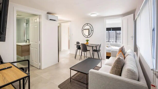 A modern living room with a sofa, a dining table with chairs, a TV, and a ceiling light.