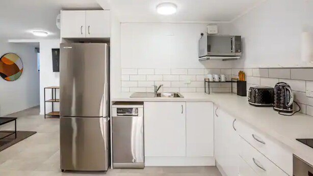 A modern kitchen with stainless steel appliances, white cabinetry, and a tiled backsplash. - Freshly Renovated Grey Lynn 3Br Unit! (Auckland)