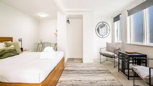 A modern hotel room with a large bed, a small desk, a chair, and a window. - Stunning Studio In Grey Lynn! (Auckland)