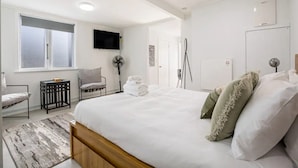 A modern bedroom with a large bed, a TV mounted on the wall, a standing fan, and a small table with a chair. - Stunning Studio In Grey Lynn! (Auckland)