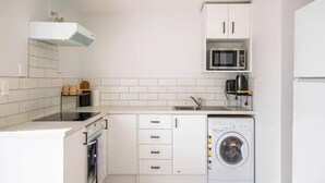 A compact kitchen with white cabinets, a microwave, a washing machine, and a stove. - Stunning Studio In Grey Lynn! (Auckland)