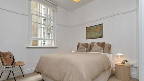 A bedroom with a large bed, a chair, a bedside table with a lamp, and a world map on the wall. - Heart Of The City Apartment In Heritage Building (Auckland)