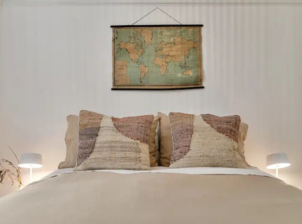 Una cama con un mapa del mundo encima, dos lámparas a cada lado y una pared sencilla.