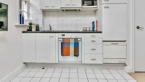 A modern kitchen with white cabinets, a microwave, a dishwasher, and a tiled backsplash. - Heart Of The City Apartment In Heritage Building (Auckland)
