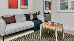 A modern living room with a grey sofa, a wooden coffee table, and a large mirror. - Heart Of The City Apartment In Heritage Building (Auckland)