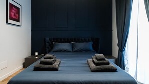 A neatly made bed with a dark headboard and pillows, a bedside table with a lamp, and a framed sign on the wall.
