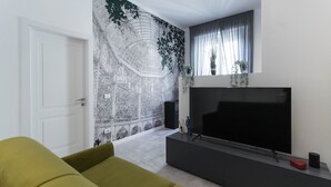Ein modernes Wohnzimmer mit einem großen schwarzen Fernseher, einem grünen Sofa und einem Wandgemälde einer Stadtansicht.