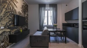 A modern kitchen with a dining area, a flat-screen TV mounted on the wall, and a window with curtains.