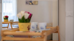 Een eetgedeelte met een houten tafel, stoelen, een bloevas en een aan de muur hangend schilderij.