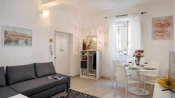 Een moderne woonkamer met een grijze bank, een eettafel met stoelen, een klein keukentje en een witte kledingkast.