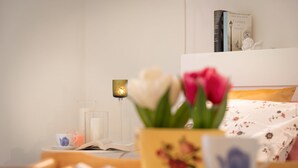 Een keurig opgemaakt slaapkamer met een nachtkastje waarop een boek, een kopje en een glas jus d’orange staan. Ook is een bedlampje en decoratief object te zien.
