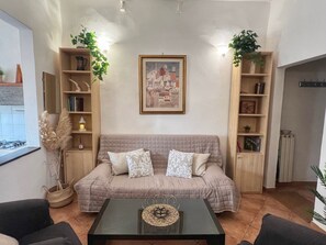 A living room with a beige sofa, a glass coffee table, and two side tables. There are bookshelves on either side of the sofa, and a framed picture hangs above it. - FI-D612-GHIB94A3 - Il Giglio Bianco (Firenze)