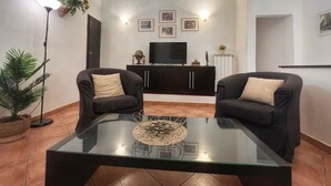 Un soggiorno con due divani scuri, un tavolino in vetro, una TV su un mobile basso e una pianta in vaso.