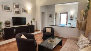 Un soggiorno con un divano, due poltrone, un tavolino da caffè, una TV e quadri appesi al muro.
