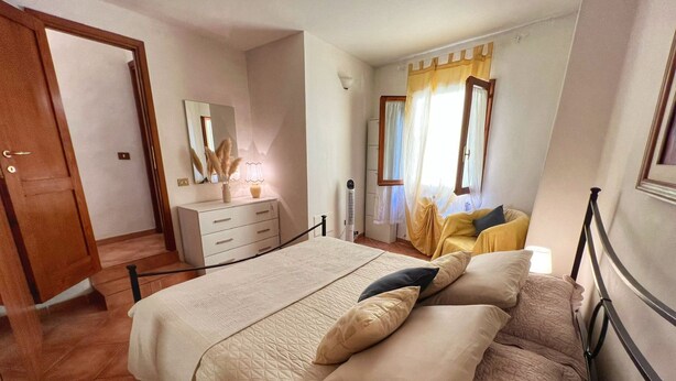 Una camera da letto con un letto, una cassettiera, uno specchio e una finestra con tende.