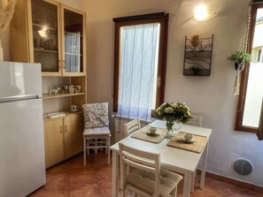 A compact kitchen with a refrigerator, wooden cabinets, a dining table with chairs, and a window with curtains. - FI-D612-GHIB94A3 - Il Giglio Bianco (Firenze)
