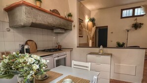Una cucina compatta con un piano di lavoro bianco, un fornello e un lavello. C'è un'area pranzo con un tavolo e sedie, e un vaso con fiori sul tavolo.