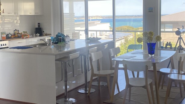 Una cocina moderna con una isla grande, armarios blancos y vista al mar.
