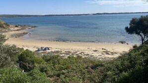 Una playa con agua cristalina, una orilla arenosa y algunas tiendas de campaña.
