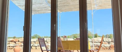 A room with a sliding glass door leading to an outdoor patio with a yellow table and chairs, a large terracotta pot, and a stone wall.