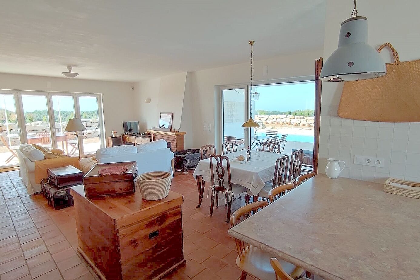 Un vaste espace de vie avec une grande fenêtre donnant sur une plage, un coin repas avec une table et des chaises, et un coin salon confortable avec un canapé et une cheminée.