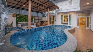 A swimming pool with a tiled edge, a covered patio area, and a two-story building with a balcony. - Gala Pavilion (Pattaya)