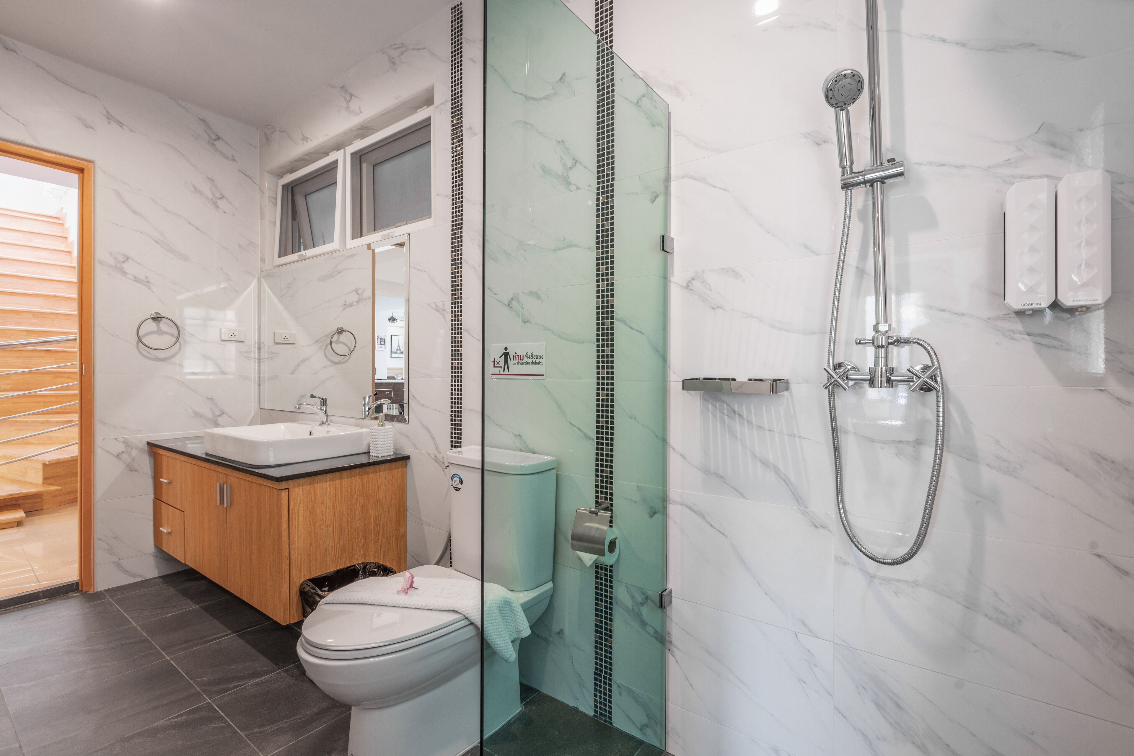 A modern bathroom with a glass-enclosed shower, a wooden vanity, and a toilet.
