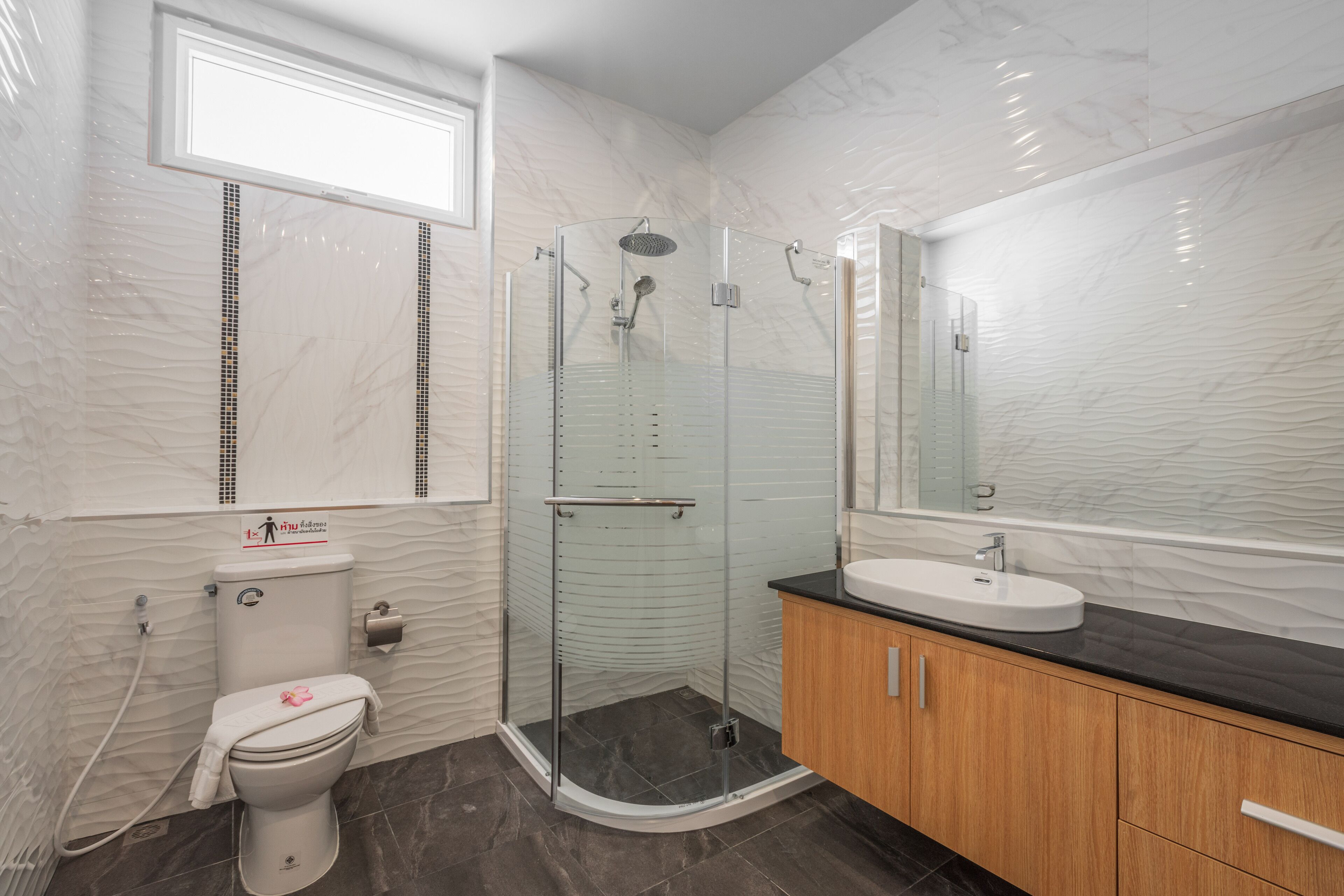 Une salle de bain moderne dotée d’une douche à parois de verre, de toilettes et d’un lavabo avec un plan de travail noir.