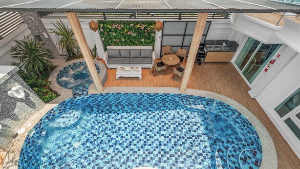 A modern indoor pool with a mosaic tile design, surrounded by a wooden deck and a seating area with a sofa and chairs. - Gala Pavilion (Pattaya)