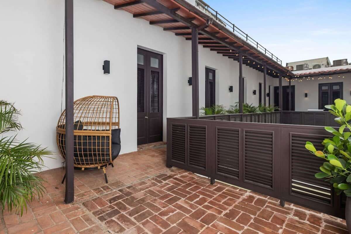 A courtyard with a brick floor, a white wall, and a wooden pergola.