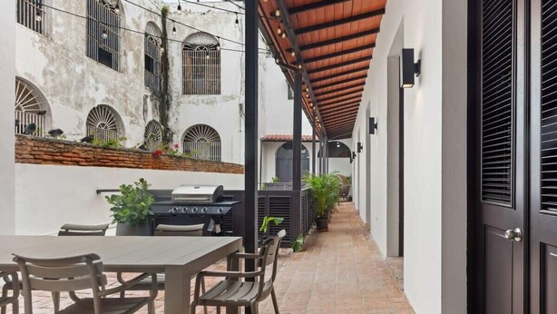 Eine überdachte Terrasse mit Grill, Sitzgelegenheiten und Topfpflanzen.