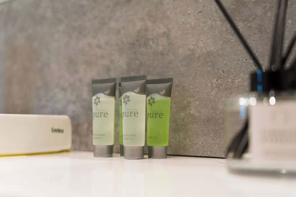 Three bottles of Pure shampoo on a white surface with a textured wall in the background.