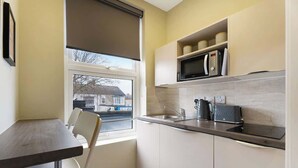 A compact kitchen with a window, a microwave, a kettle, and a small dining area. - Luxurious 1 Bedroom with Private Parking and Wifi (Middlesbrough)