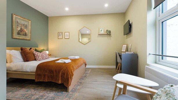 A bedroom with a bed, bedside table, desk, chair, and a large window. - Luxurious 1 Bedroom with Private Parking and Wifi (Middlesbrough)
