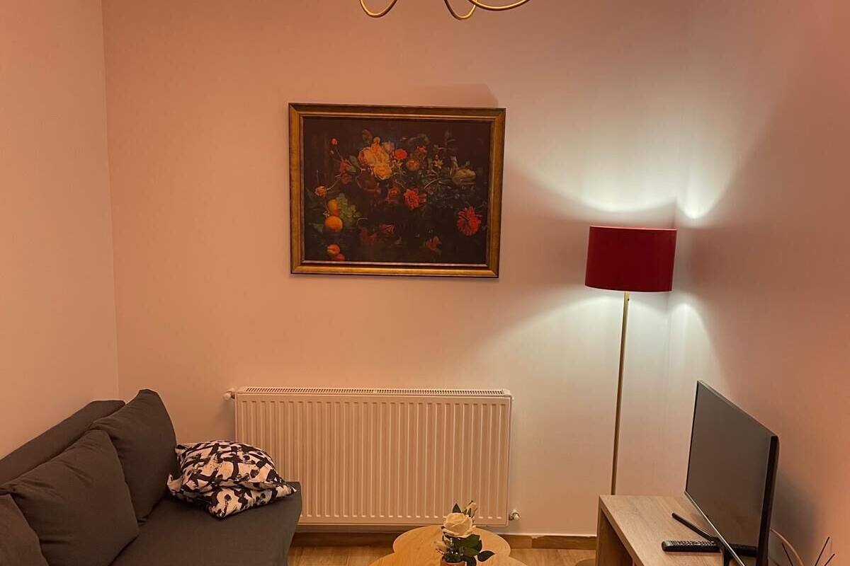 Una sala de estar con un sofá, una mesa de centro, un televisor, un cuadro y una lámpara de pie.