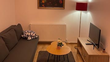 Una sala de estar con un sofá, una mesa de centro, un televisor, un cuadro y una lámpara de pie.