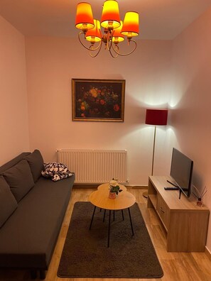 Una sala de estar con un sofá, una mesa de centro, un televisor, un cuadro y una lámpara de pie.
