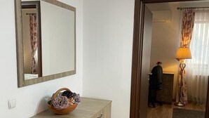 Une pièce avec un meuble en bois, un miroir et une porte qui donne sur une autre pièce, où se trouvent une lampe et des rideaux.