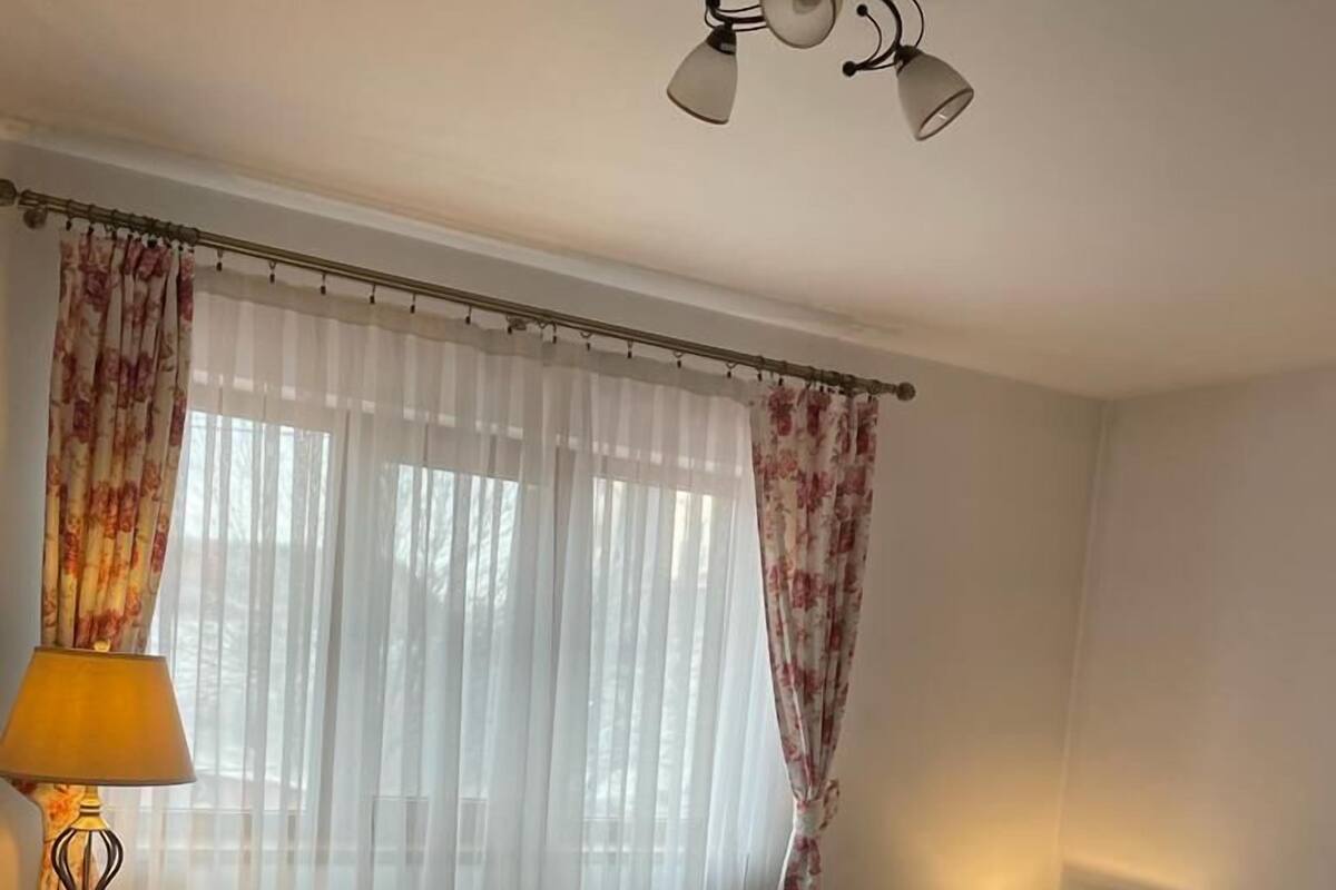 Habitación de hotel con cama, lámpara, luz en el techo y ventana con cortinas.