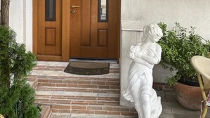 Une porte d’entrée en bois avec un petit auvent, une allée dallée de pierres et une statue blanche représentant une figure.