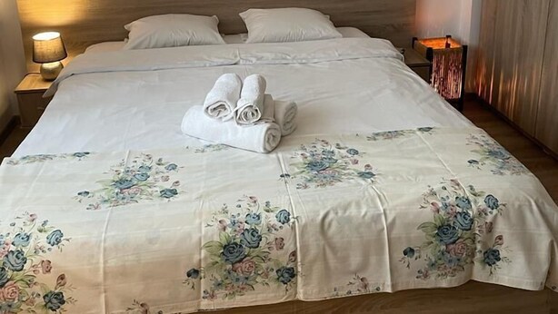 Un lit bien fait, avec une literie à motifs floraux, deux serviettes enroulées et une lampe de chevet.