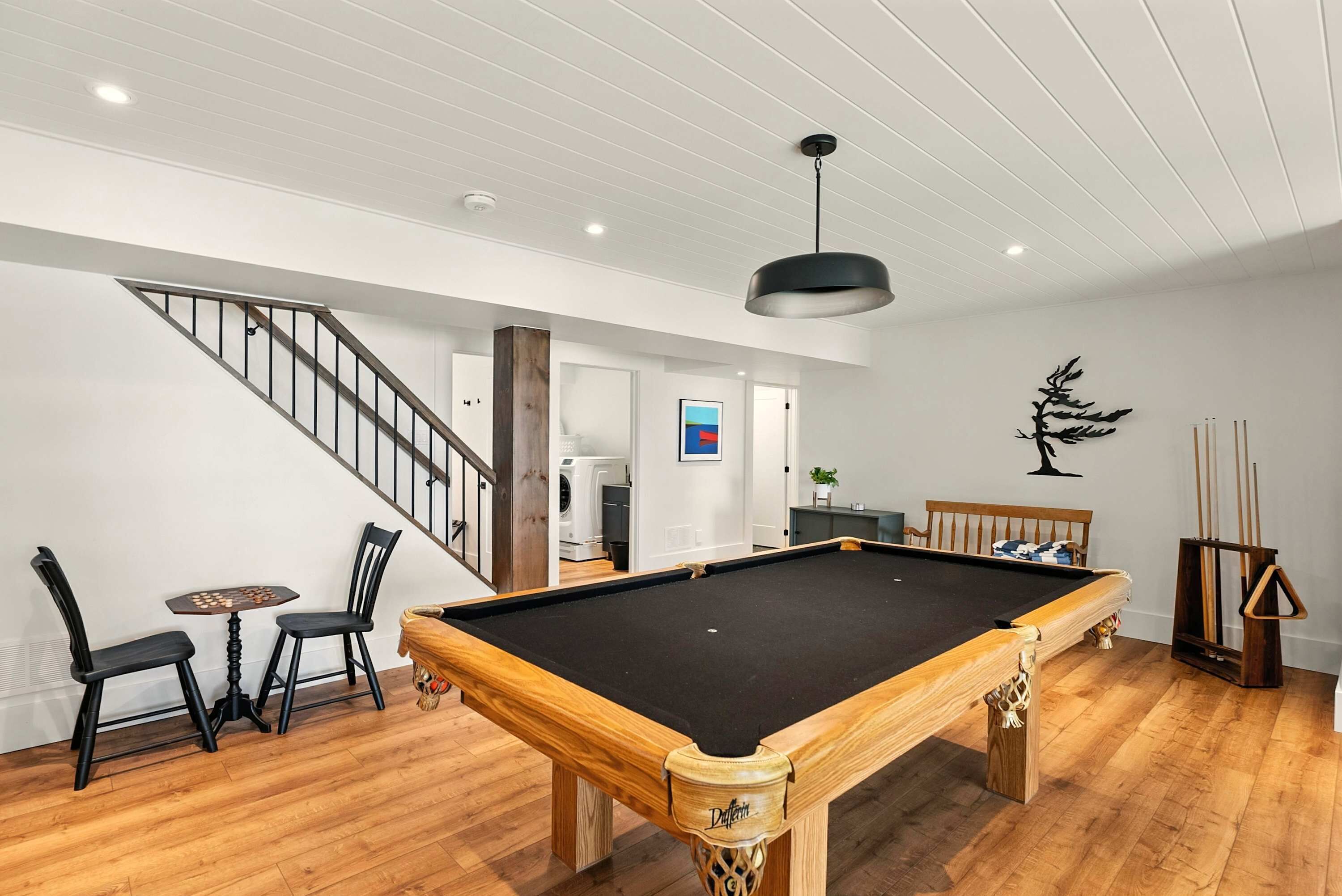A pool table in a room with wooden flooring, a staircase, and a ceiling with recessed lighting.