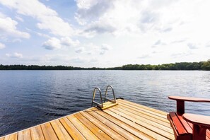 A wooden dock extending into a calm lake with a metal ladder and a red bench.