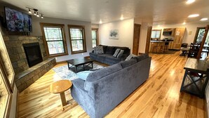 A spacious living room with a stone fireplace, a sectional sofa, a coffee table, and a wooden floor. - Wooded Bliss @ Spring Brook Resort (Wisconsin Dells)