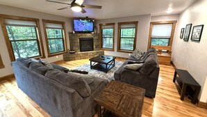 A living room with a fireplace, large windows, a ceiling fan, and a television. - Wooded Bliss @ Spring Brook Resort (Wisconsin Dells)