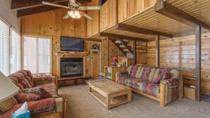 Interior acogedor de una cabaña con detalles de madera, una chimenea, un sofá, una mesa de centro y un ventilador de techo.