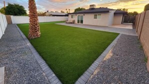 Un jardin avec une pelouse artificielle, un palmier et une maison avec un garage.