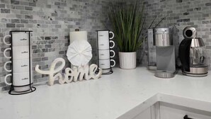 Une cuisine avec des meubles blancs, un coin café, une plante en pot et une machine à café.